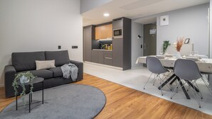 Una sala de estar moderna con un sofá gris, una mesita auxiliar con una planta y un comedor con una mesa para dos.
