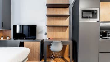 A compact hotel room with a bed, a TV, a desk with a chair, a microwave, and a small kitchenette.