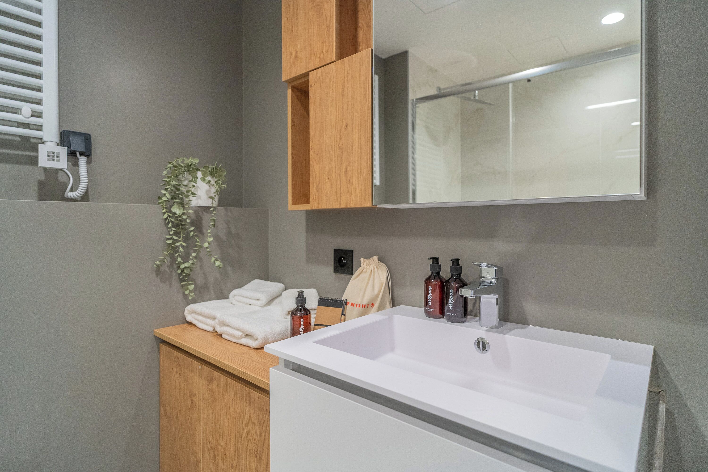Un baño con lavamanos blanco, armarios de madera, un espejo, un perchero para toallas y una planta.