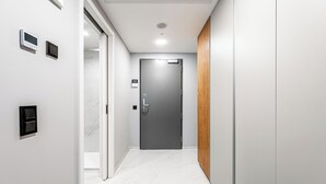 Un pasillo con suelo de mármol, una puerta gris y un panel de madera en la pared derecha.