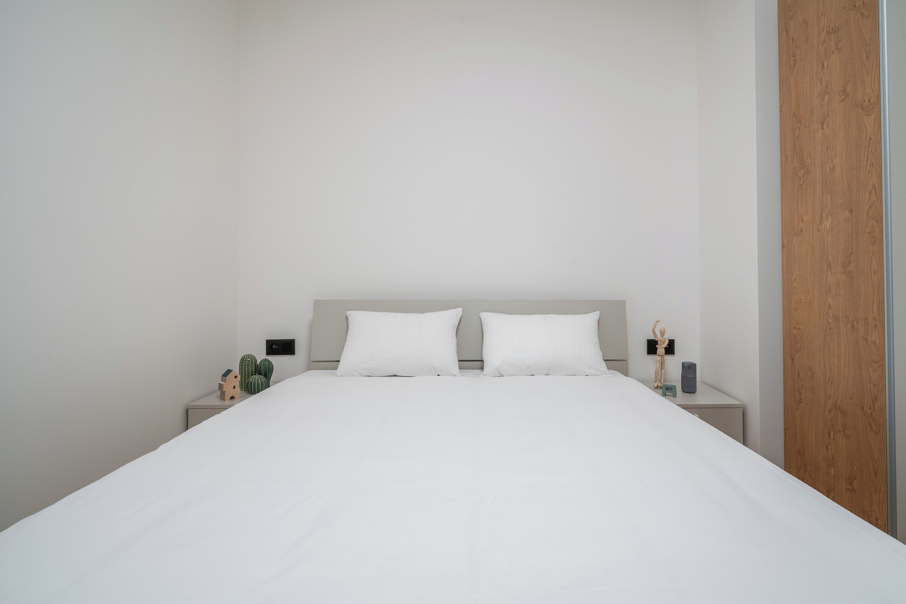 A minimalist bedroom with a large bed, two bedside tables, and a wooden panel on one wall.