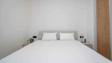 A minimalist bedroom with a large bed, two bedside tables, and a wooden panel on one wall.