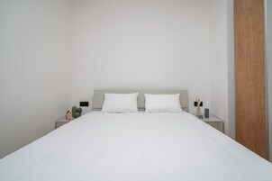 Un dormitorio minimalista con una cama grande, dos mesitas de noche y un panel de madera en una pared.
