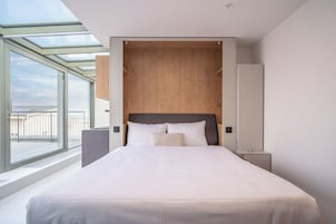 Una camera d'albergo moderna con un letto grande, una testiera in legno, un comodino e un'ampia finestra con vista sulla spiaggia.