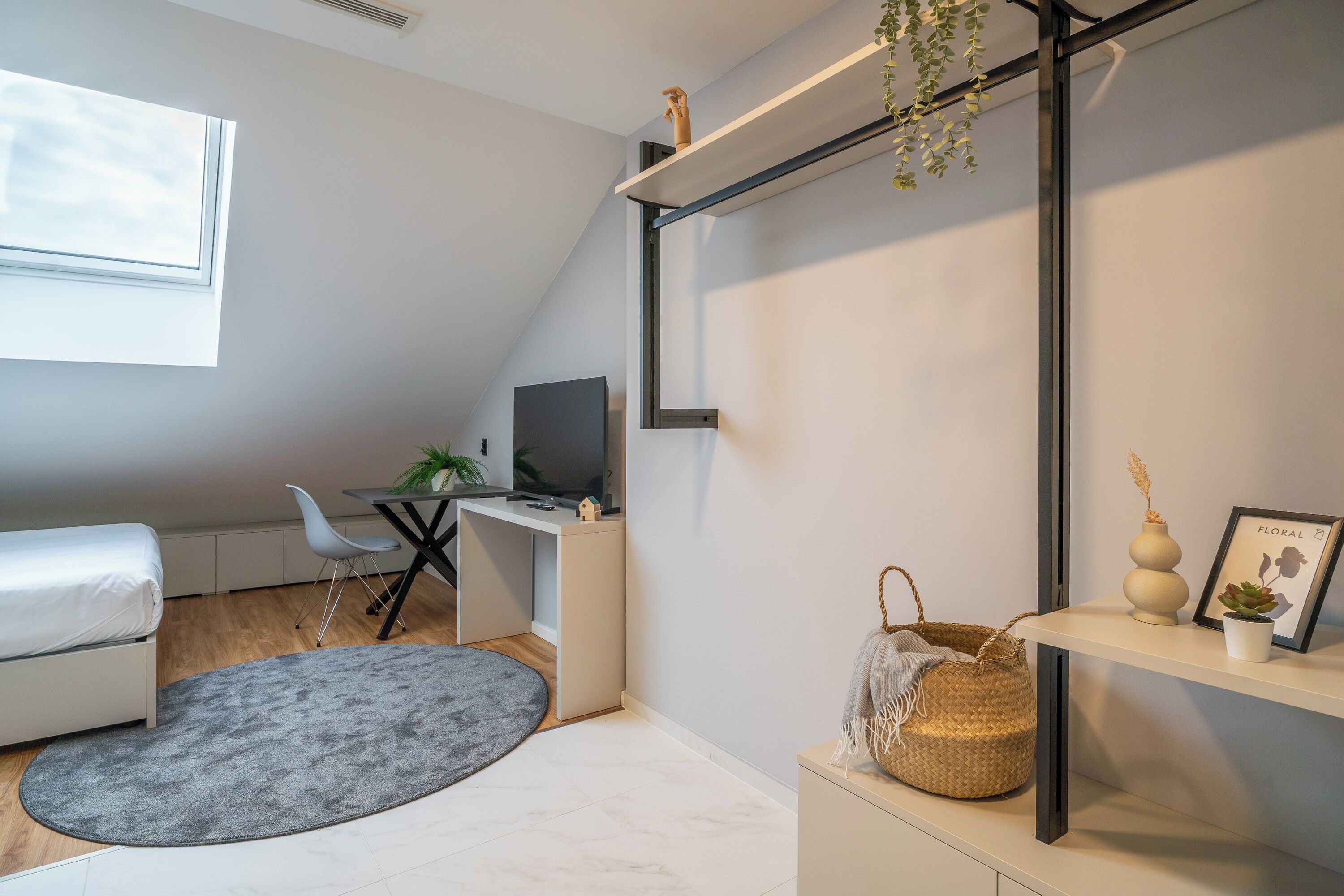 Un dormitorio moderno con cama, escritorio y silla, un tapete gris y una estantería con objetos decorativos.