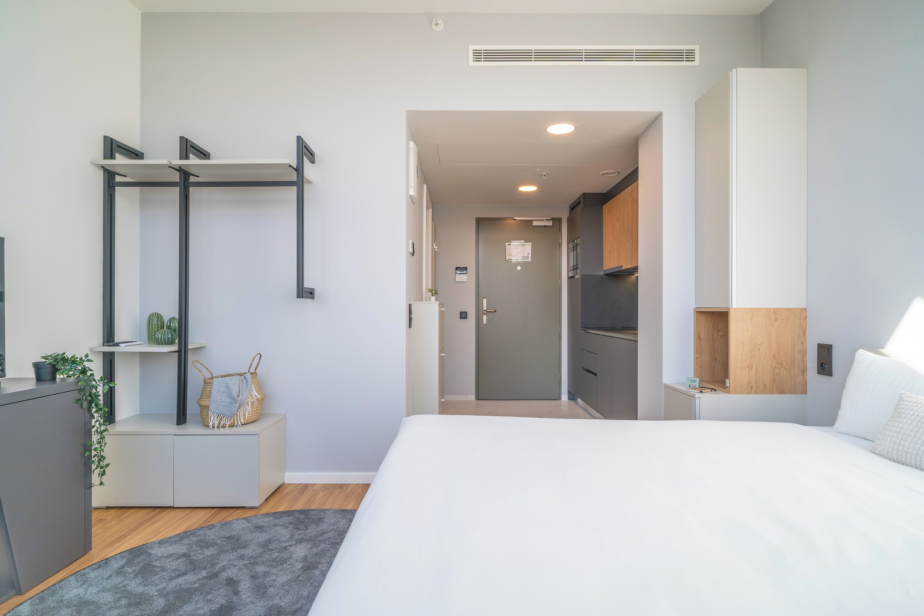 Ein modernes Schlafzimmer mit einem großen Bett, einem Schreibtisch mit Stuhl, einem Kleiderschrank und einer kleinen Pflanze.