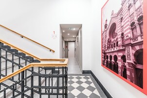 Un pasillo con piso a cuadros, una escalera con barandillas negras y escalones de madera, y un mural grande de un edificio.