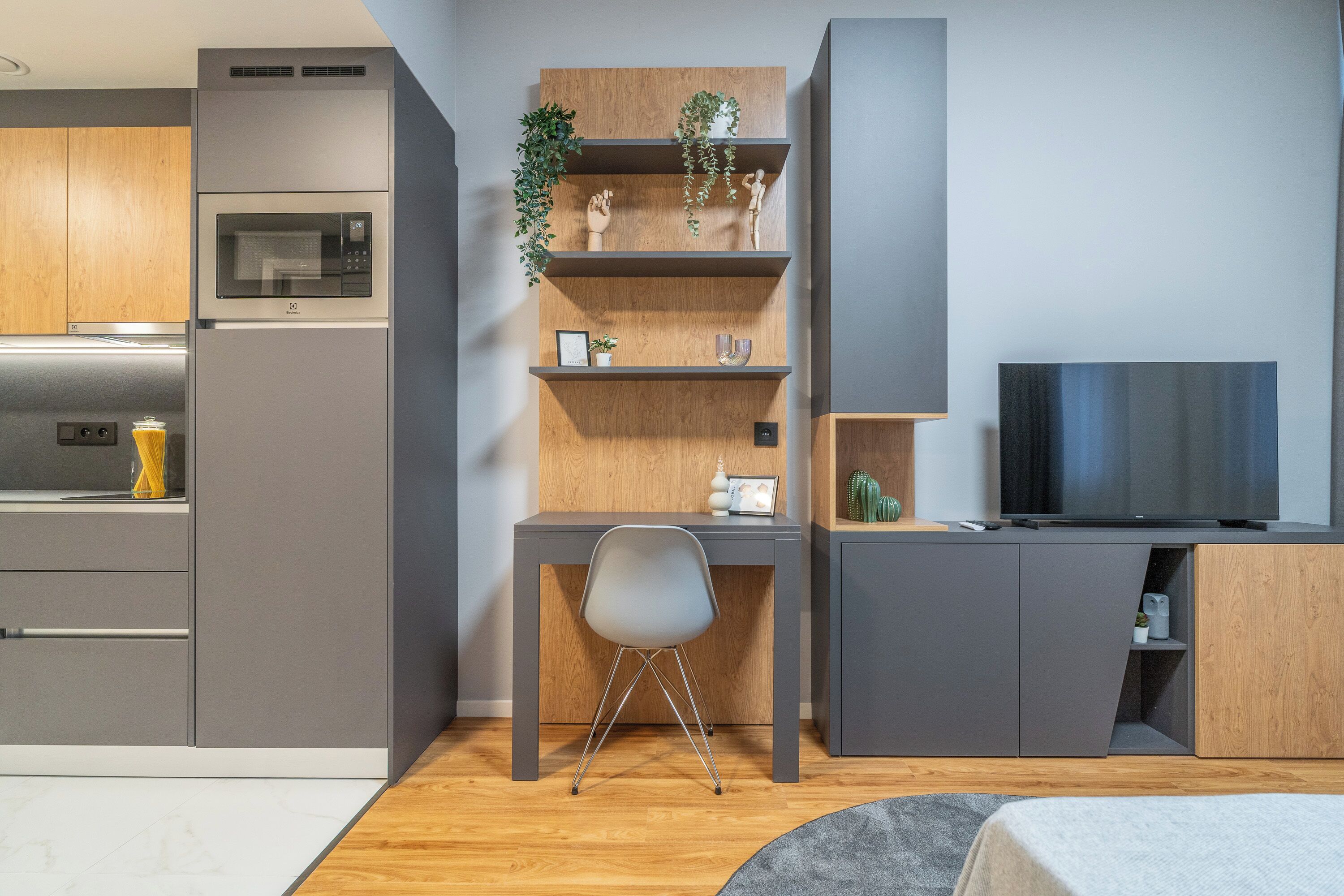 Una cocina moderna con electrodomésticos integrados, un escritorio de madera con estantes, una silla y un televisor.