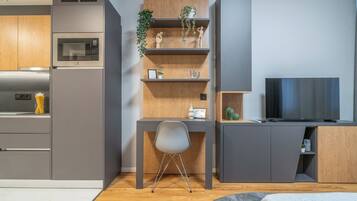 Une cuisine moderne dotée d’appareils électroménagers intégrés, un bureau en bois avec des étagères, une chaise et un téléviseur.