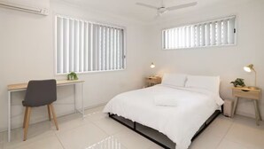 Ein Schlafzimmer mit einem Bett, einem Schreibtisch, einem Stuhl, zwei Nachttischen mit Lampen und einem Deckenventilator.