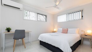 A bedroom with a bed, bedside tables, a desk, a chair, and a ceiling fan.
