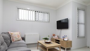 A modern living room with a grey sofa, a wooden coffee table, a TV mounted on the wall, and a small cabinet with decorative items.