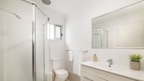 Een moderne badkamer met een douchecabine van glas, een wit toilet, een wastafel met spiegel en een kleine potplant.