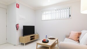 Un salon moderne avec un téléviseur à écran plat, une table basse en bois, un canapé et une petite table d’appoint.