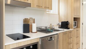 Une cuisine moderne avec des meubles en bois, un lave-vaisselle Bosch, une machine à café noire et un bloc à couteaux.
