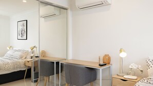 Une chambre à coucher moderne, comprenant un lit, un bureau, deux chaises, une table de chevet et un miroir.