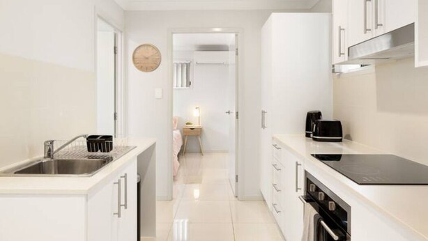A modern kitchen with white cabinetry, a black induction cooktop, and a stainless steel sink.
