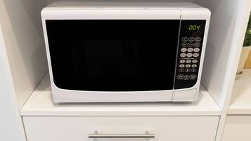 Un four à micro-ondes est posé sur une étagère d’un meuble blanc, et un tiroir situé en dessous contient une casserole et une poêle.