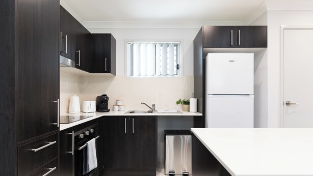 Una cocina moderna con armarios oscuros, un refrigerador de acero inoxidable y una encimera blanca.
