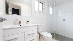 Un baño moderno con tocador blanco, inodoro y cabina de ducha de vidrio.