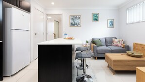 Una cocina moderna con un refrigerador blanco, una isla negra y un sofá gris con una mesita de madera.