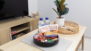 A room with a television, a plant, a basket with snacks, and a water bottle on a table. - Clean 1 Bdr Apt w/ AC & Kitchen | Parking | 139F1 (Rocklea)