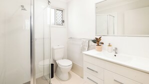 Un bagno moderno con cabina doccia in vetro, un water, un lavandino con specchio e una piccola finestra.