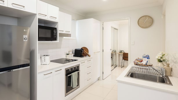 Una cocina moderna con armarios blancos, un refrigerador de acero inoxidable, un microondas, un tostador y un lavamanos.