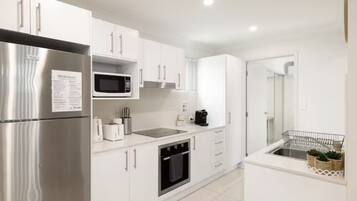 A modern kitchen with white cabinetry, stainless steel appliances, a microwave, a coffee maker, and a small sink with a dish rack.