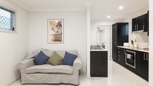 Een moderne woonkamer met een bank, een keuken met donkere kastjes en een ingelijste foto aan de muur.