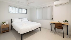 Een slaapkamer met een bed, een bureau, een stoel, een plafondventilator en een airconditioning.