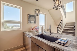 A kitchen with a large island, a double sink, and a view of the city. There is a staircase leading to an upper level. - Casa de Luz: Modern Oasis with Desert Views (Grand Junction)
