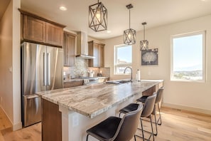 A modern kitchen with a large island, stainless steel appliances, and pendant lighting. - Casa de Luz: Modern Oasis with Desert Views (Grand Junction)