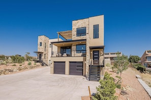 A modern two-story house with a stone facade, large windows, and a spacious driveway. - Casa de Luz: Modern Oasis with Desert Views (Grand Junction)