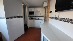 Une cuisine compacte avec des meubles blancs, un pare-feu en carreaux et un téléviseur à écran plat fixé au mur.
