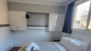 Une chambre d’hôtel avec un lit, des rideaux blancs, une fenêtre et un sol carrelé.
