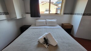 Un lit bien fait, avec des draps et des oreillers blancs, une télécommande et un smartphone posés sur une couverture à motifs.