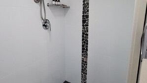 Un petit espace douche fermé, doté d’un sol carrelé noir, d’un mur blanc orné d’une bande de mosaïque noire et blanche, et d’un pommeau de douche fixé au mur.