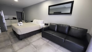Une chambre d’hôtel moderne avec un lit, un canapé en cuir noir, une petite table et un miroir au mur.