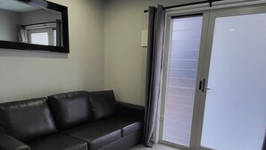Un salon avec un canapé en cuir noir, un grand miroir et une porte-fenêtre coulissante donnant sur un balcon.