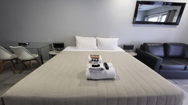 Une chambre d’hôtel avec un lit bien fait, un coin salon avec un canapé et des fauteuils, une petite table avec une lampe et un grand miroir au mur.