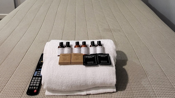 A hotel room with a bed, a remote control, and a tray of makeup products. - Jesmond Small Studio (Jesmond)