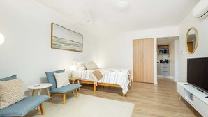 Una habitación de hotel moderna con una cama, dos sofás, un televisor y una cocina al fondo.