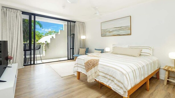 Un dormitorio con cama, escritorio, silla, lámpara y vistas al exterior.