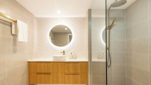 Un baño moderno con ducha de vidrio, un espejo redondo y muebles de madera.