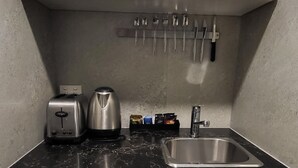 Een kleine keuken met witte kastjes, een zwart aanrecht, een roestvrijstalen spoelbak, een broodrooster, een waterkoker en een magnetron.