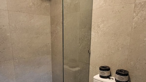 Een moderne badkamer met een douche met glazen wand, een wit toilet en twee vuilnisbakken op de tank.