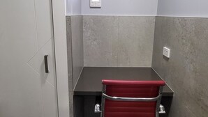 Een kleine kantoorruimte met een bureau, stoel en een airconditioner aan de muur.