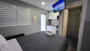 Een hotelkamer met een bed, een aan de muur bevestigde televisie, een badkamer en een kitchenette.