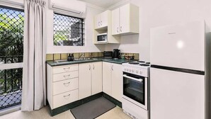 Une cuisine de taille réduite, avec des meubles blancs, une cuisinière, un four à micro-ondes et un réfrigérateur.